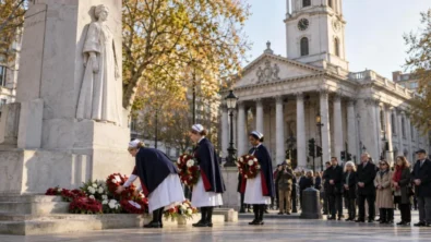Nurses in traditional capes lay red and white wreaths at the Edith Cavell memorial on St Martin's Place, with St Martin-in-the-Fields behind