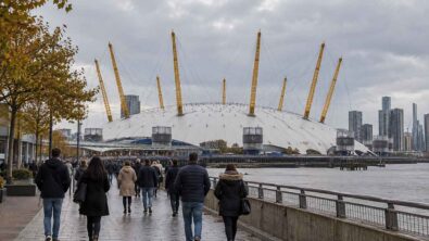 People in autumn coats walking beside the Thames with The O2 dome beyond