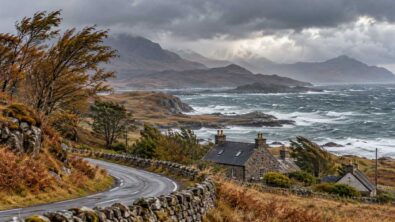 A coastal road and stone houses beneath cloudy skies in a Scottish-style landscape